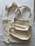 Two beige cloth bags with handles laid flat on a slightly crumpled fabric surface. The bags have a simple, unadorned design and appear to be made of cotton or canvas material.