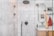A modern bathroom with marble walls and a sleek, black showerhead. The shower area features built-in niches for toiletries. Outside the shower, there is a circular mirror, a wooden vanity with a white countertop, and a red towel hanging nearby. A wooden bath brush is seen hanging inside the shower enclosure.