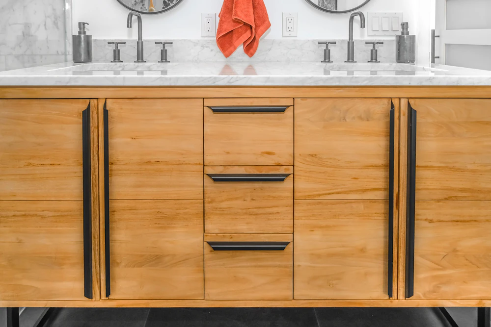 Timber bathroom vanity with black handles and a pale countertop. Stock image, placeholder.