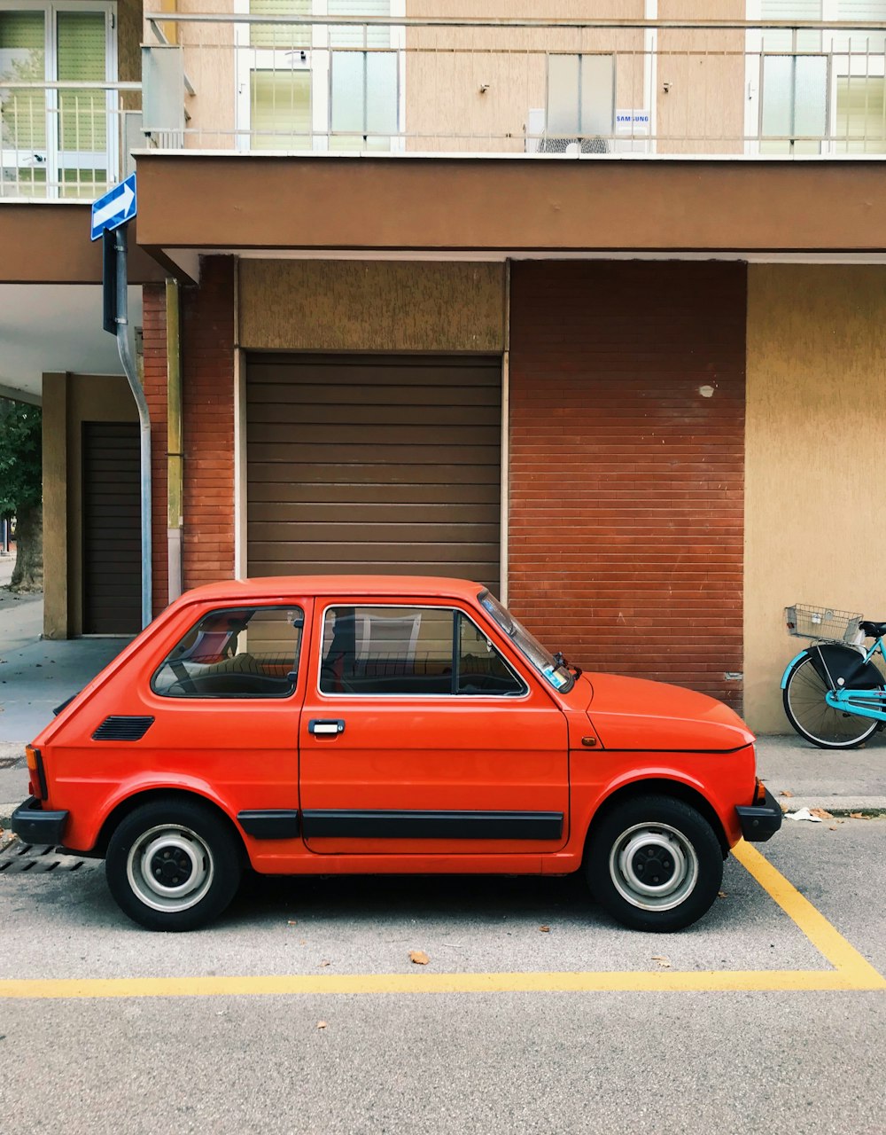 red 5 door hatchback parked beside brown building during daytime