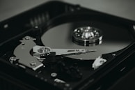 An open hard disk drive is displayed with its reflective magnetic disk and reading arm visible. The intricate mechanical components are showcased in a detailed manner, highlighting the precision of the hardware.