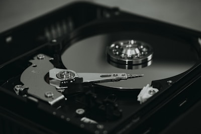 An open hard disk drive is displayed with its reflective magnetic disk and reading arm visible. The intricate mechanical components are showcased in a detailed manner, highlighting the precision of the hardware.