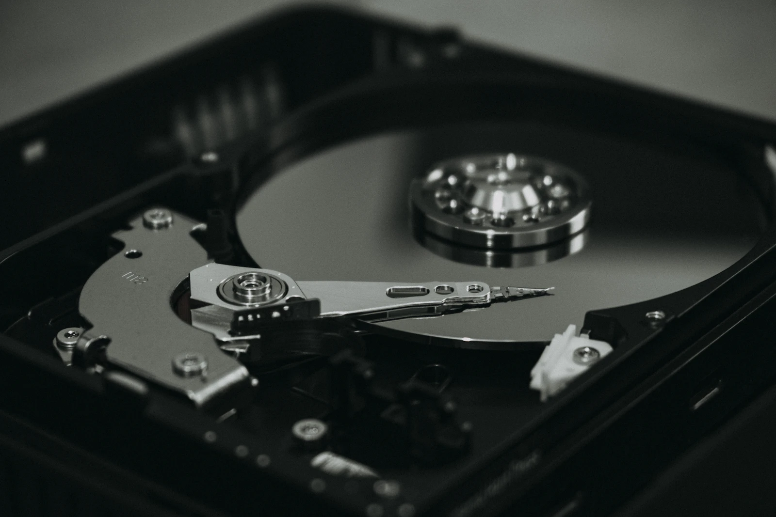Close-up of an open hard disk drive showing its internal platter, read/write arm, and spindle motor, in black-and-white tones with no visible branding or text