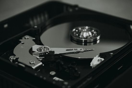 An open hard disk drive is displayed with its reflective magnetic disk and reading arm visible. The intricate mechanical components are showcased in a detailed manner, highlighting the precision of the hardware.