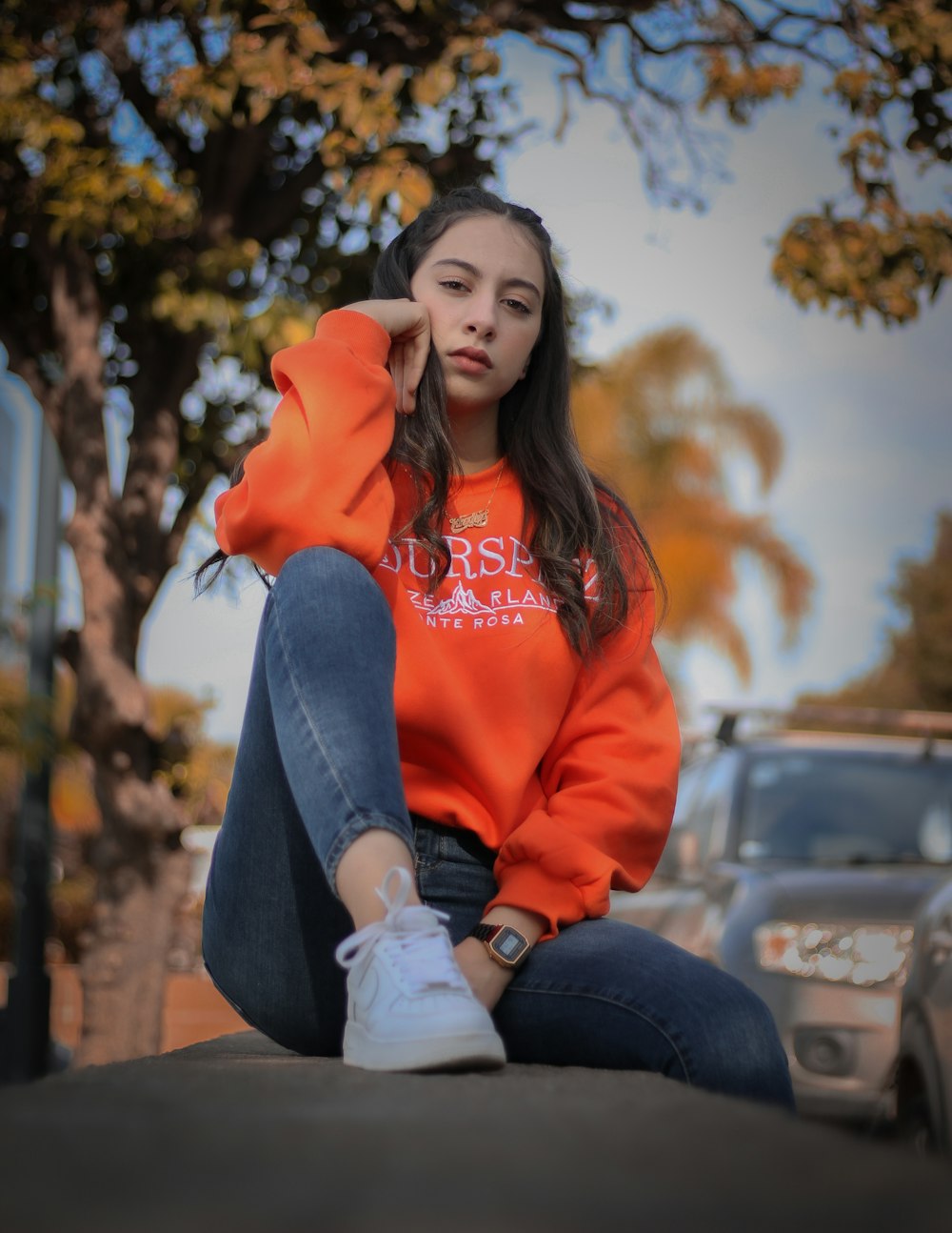 woman in red hoodie and blue denim jeans sitting on gray concrete bench during daytime