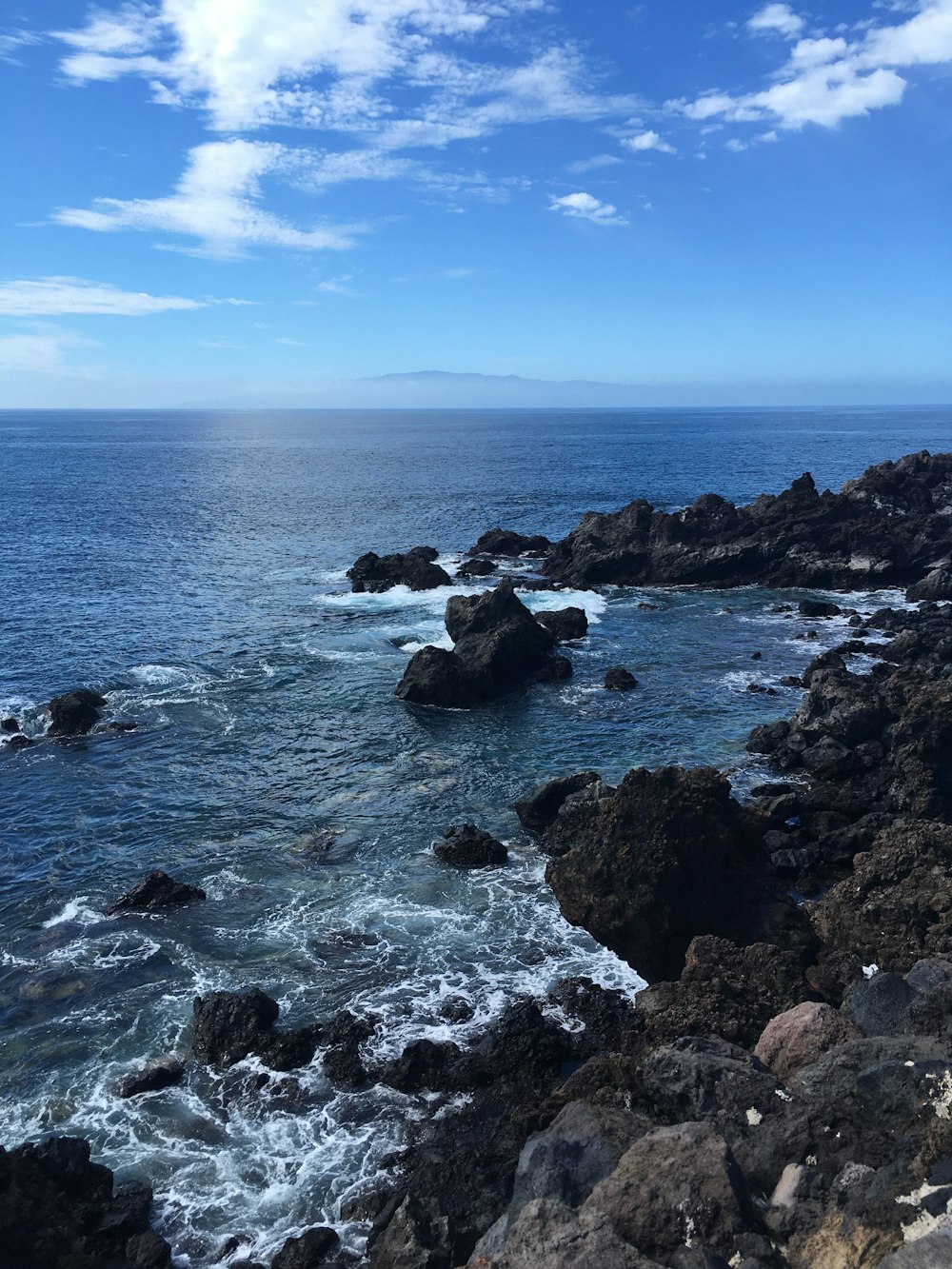 black rocks on sea under blue sky during daytime