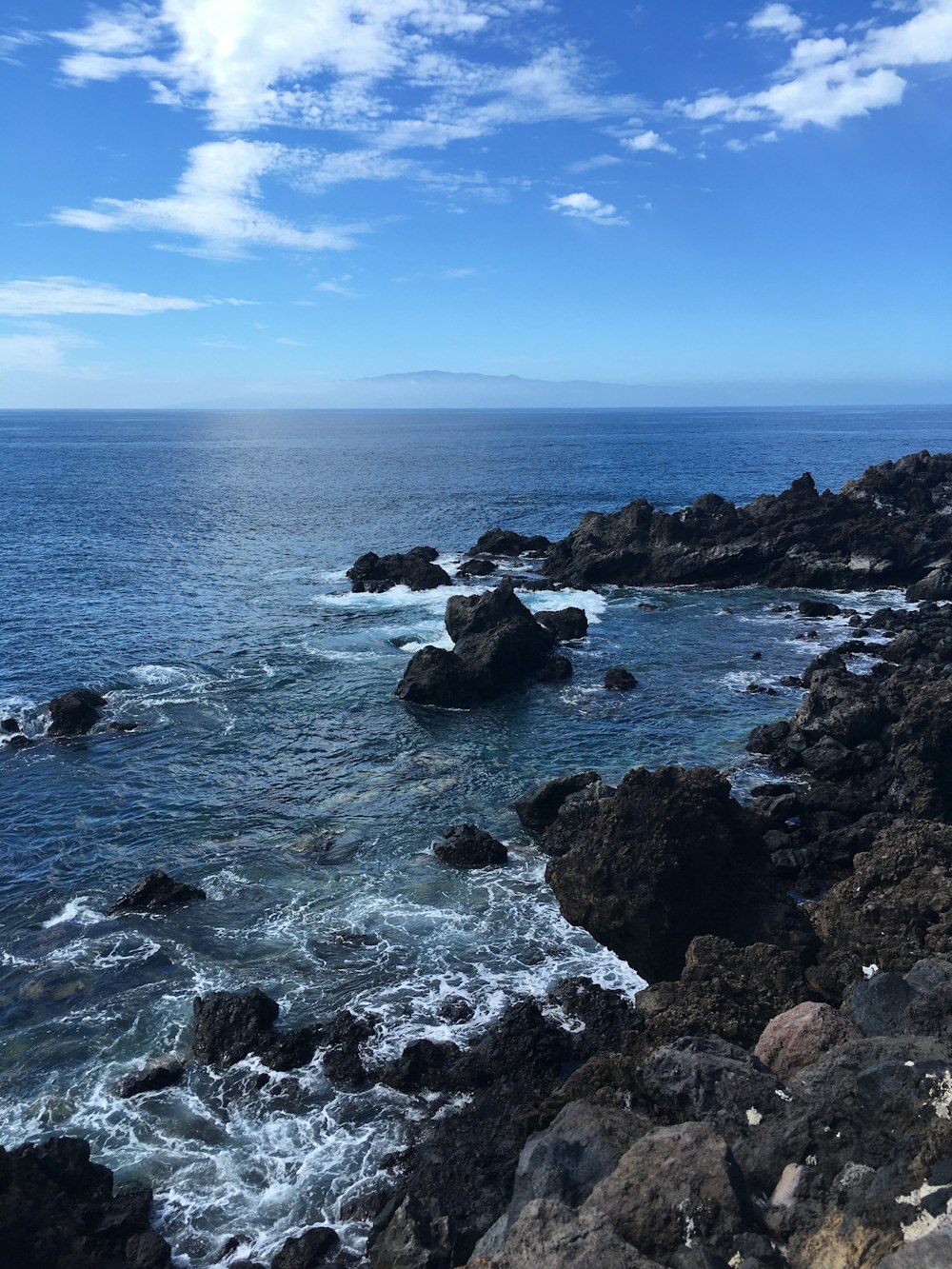 rochas negras no mar sob o céu azul durante o dia