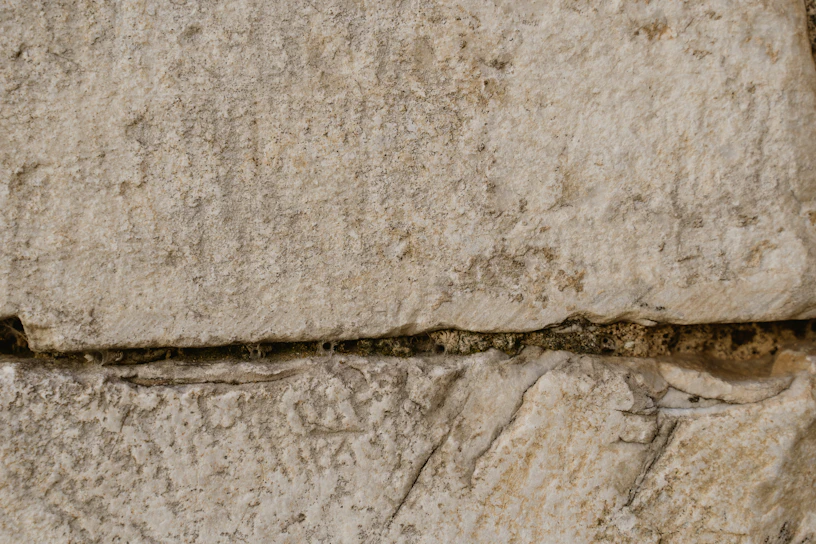 Close-up of a skilled mason carefully laying natural stone blocks on a rustic wall under bright sunlight.