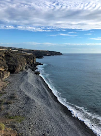 brown rocky mountain beside blue sea under blue sky during daytime