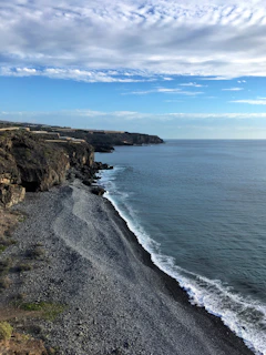 brown rocky mountain beside blue sea under blue sky during daytime