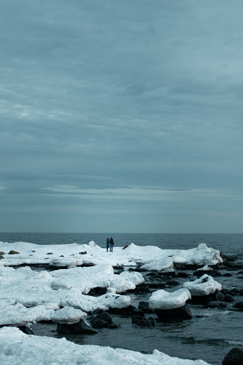 person standing on white snow covered rock formation near body of water during daytime