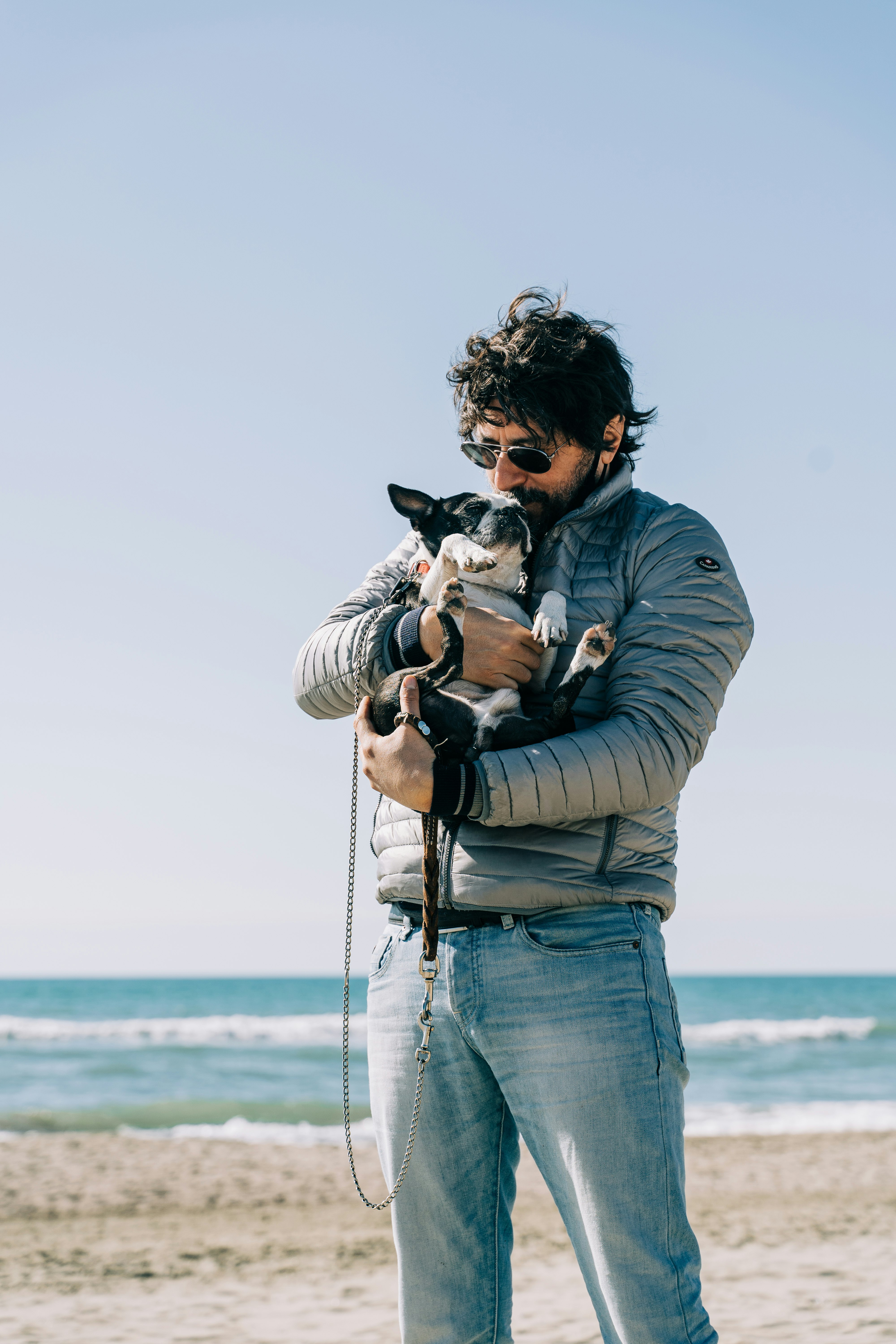 woman in gray jacket carrying black and white short coated dog