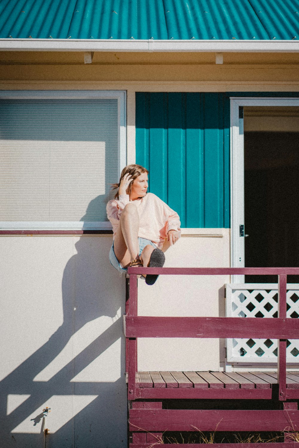 woman in white long sleeve shirt sitting on red wooden fence during daytime