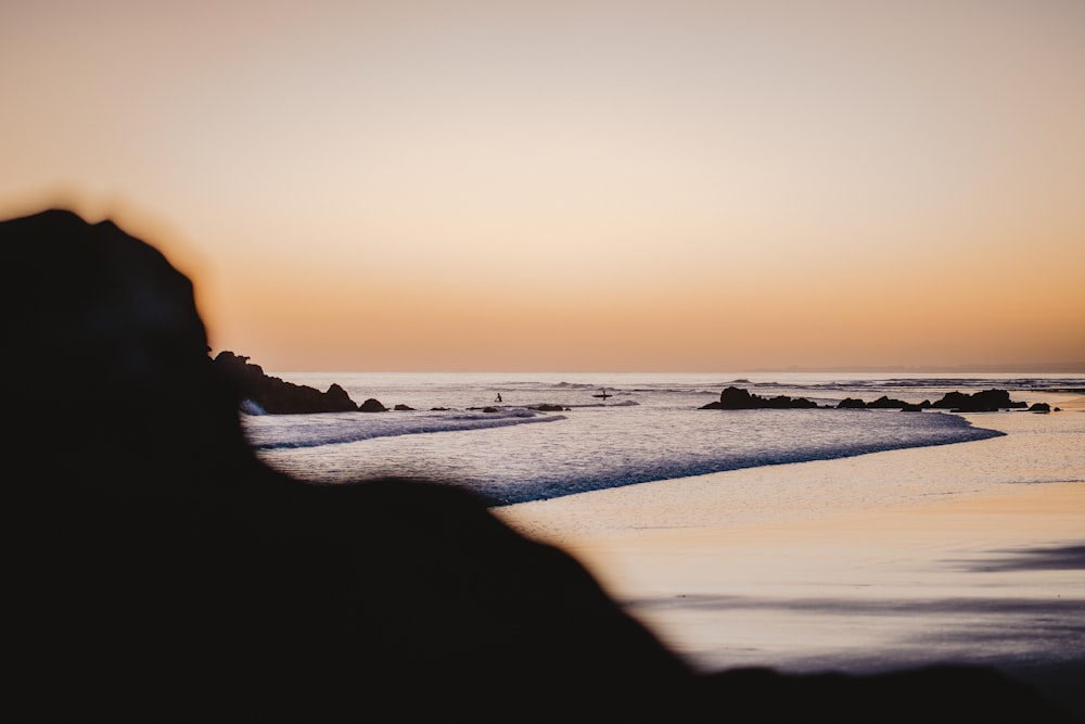 silhouette de personne debout sur le bord de mer pendant le coucher du soleil