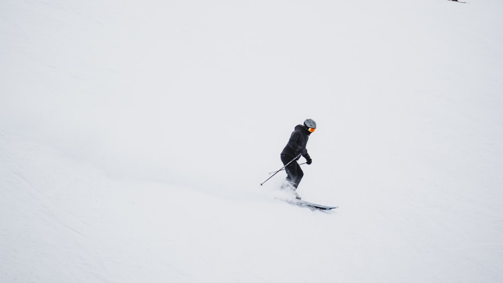검은 재킷과 검은 바지를 입은 남자가 낮에 눈 덮인 땅에서 스키 블레이드를 타고 있다