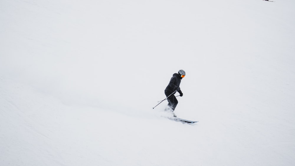 man in black jacket and black pants riding ski blades on snow covered ground during daytime