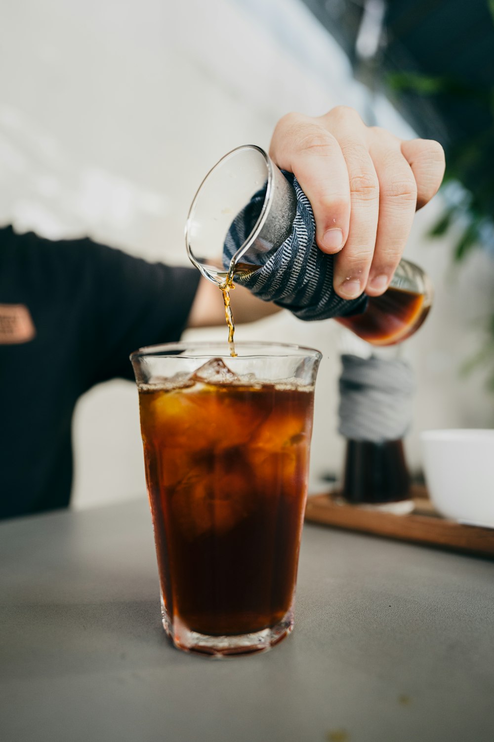 person pouring brown liquid on clear drinking glass