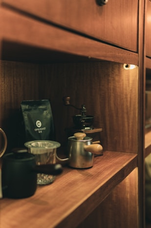 stainless steel teapot beside clear glass mug on brown wooden table