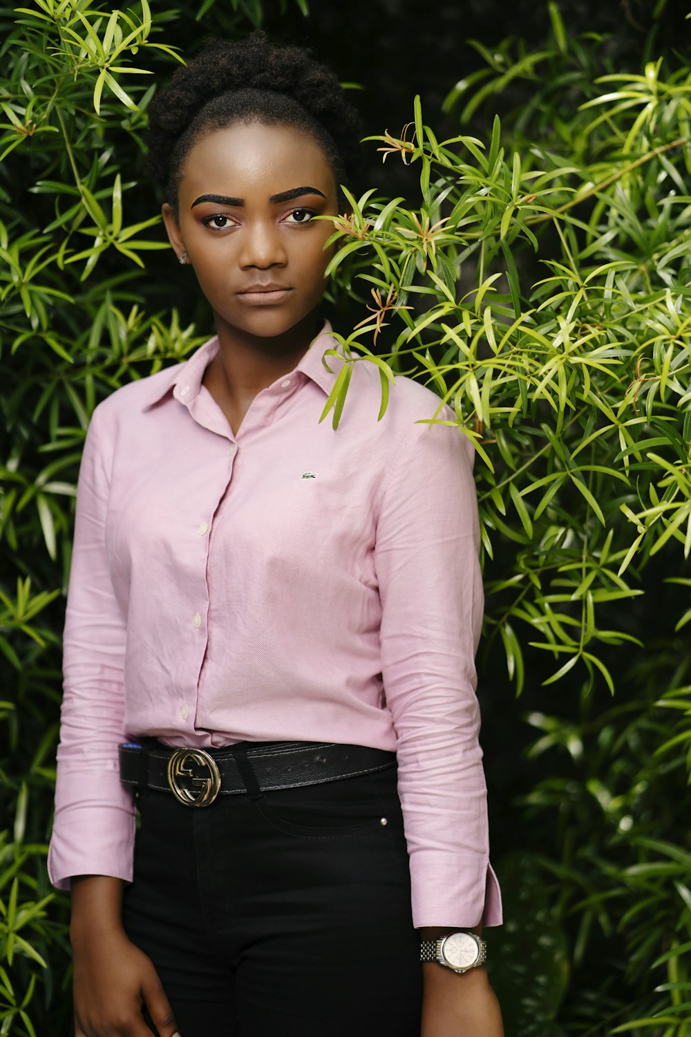 woman in pink dress shirt and black pants standing near green plants during daytime