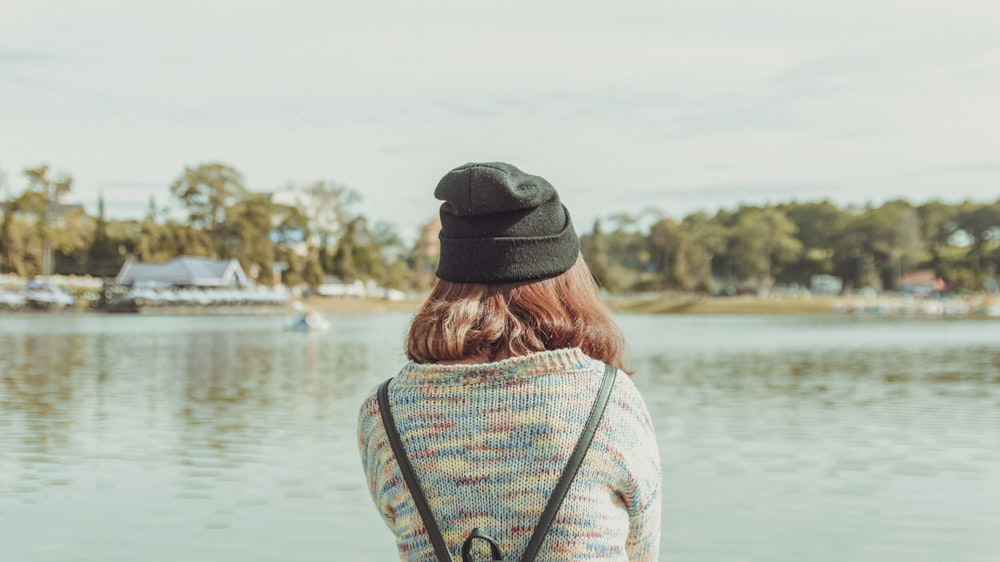 woman in white and black striped shirt and black knit cap standing near body of water