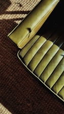 A green upholstered chair with a smooth, textured surface is partially visible on the edge of a brown carpeted floor. The lighting creates shadows and highlights on both the seat and the carpet, adding depth to the textures.