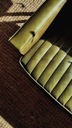 A green upholstered chair with a smooth, textured surface is partially visible on the edge of a brown carpeted floor. The lighting creates shadows and highlights on both the seat and the carpet, adding depth to the textures.