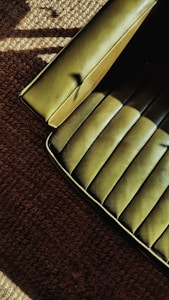 A green upholstered chair with a smooth, textured surface is partially visible on the edge of a brown carpeted floor. The lighting creates shadows and highlights on both the seat and the carpet, adding depth to the textures.