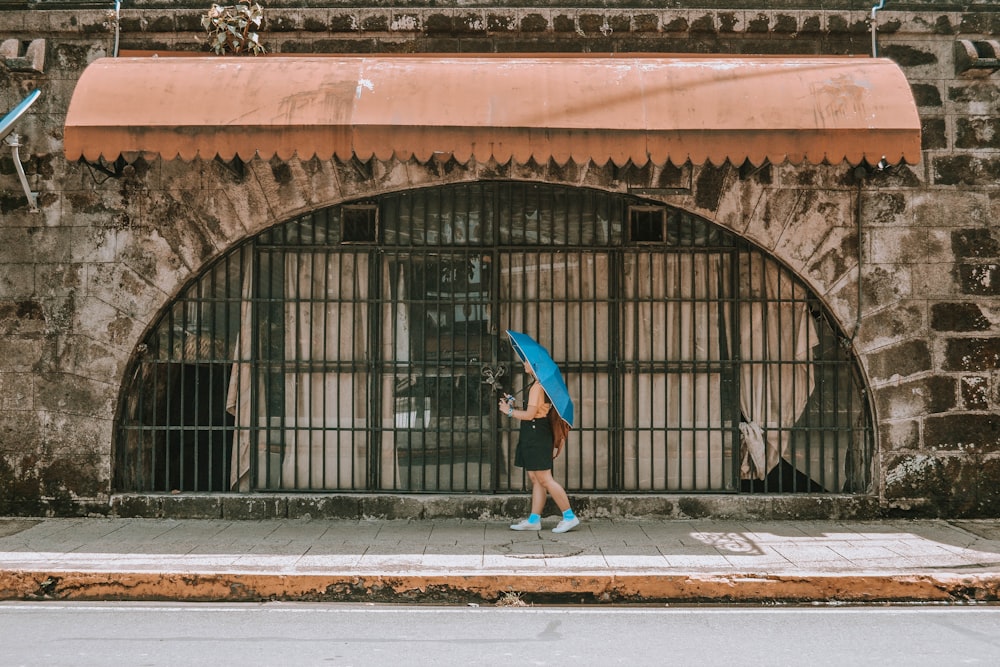 woman in blue jacket walking on sidewalk during daytime