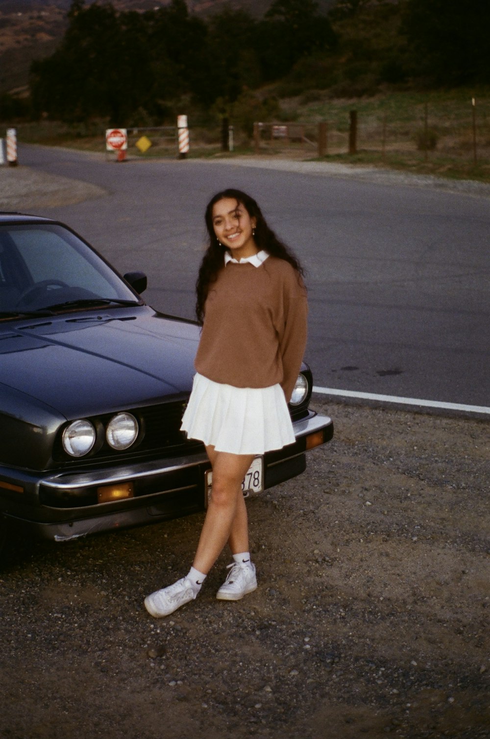 woman in brown long sleeve shirt and white skirt standing beside black bmw car