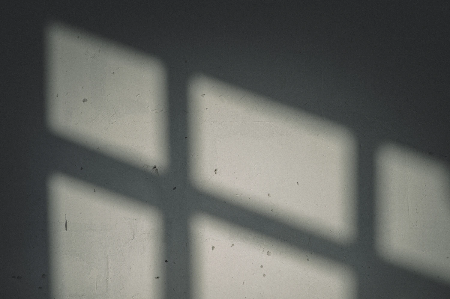 A plastered wall with the shadow of a window frame falling across it
