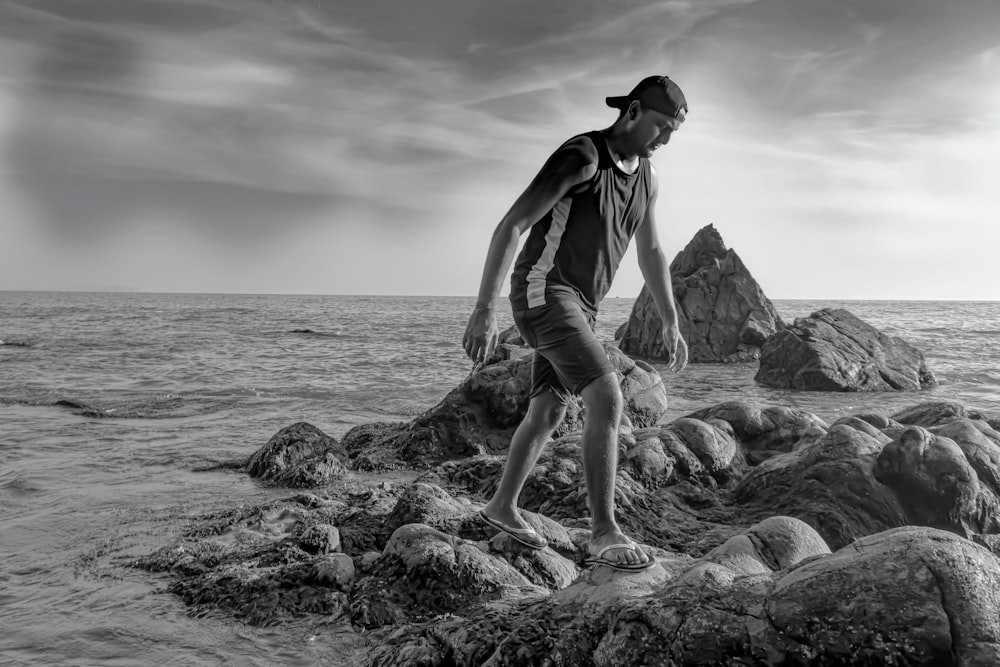 woman in black tank top and black shorts sitting on rock formation in grayscale photography