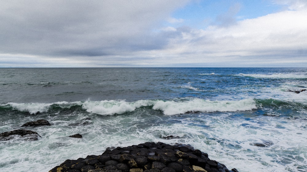 Olas del océano rompiendo contra rocas bajo nubes blancas durante el día