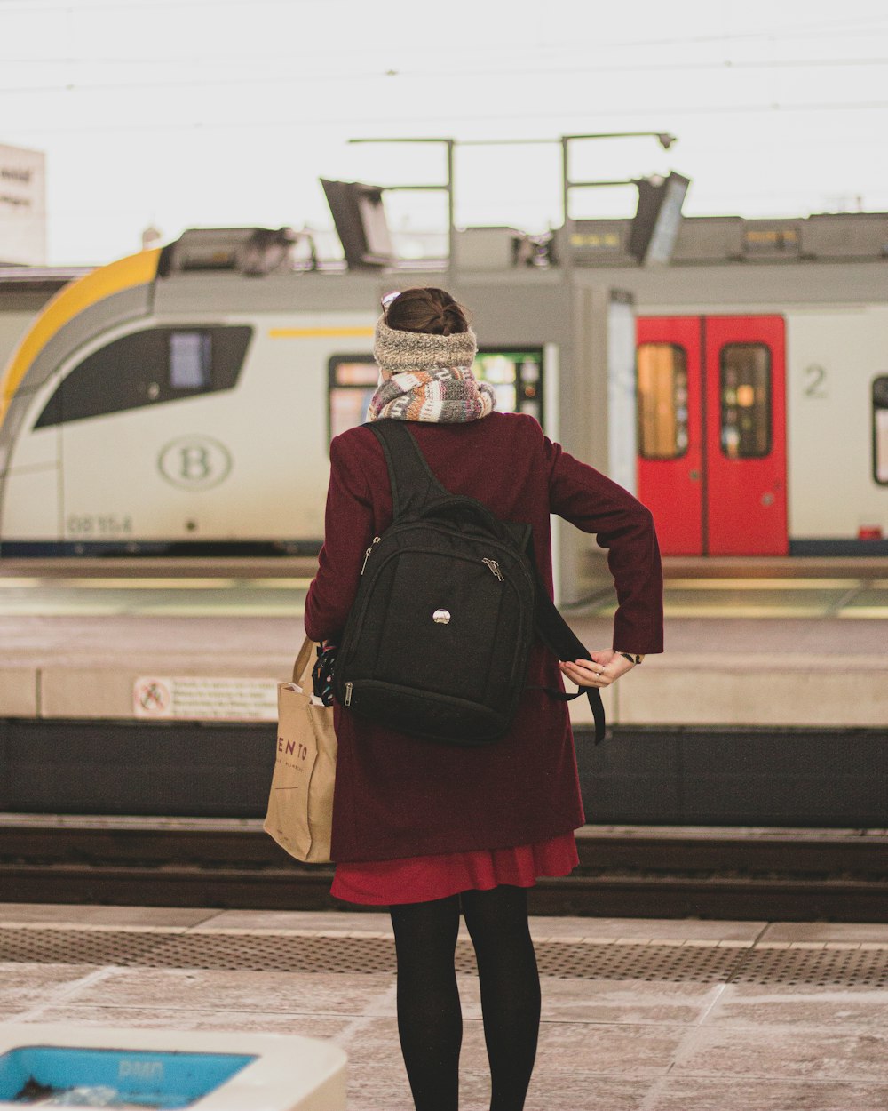 Frau in schwarz-roter Jacke steht am Bahnhof