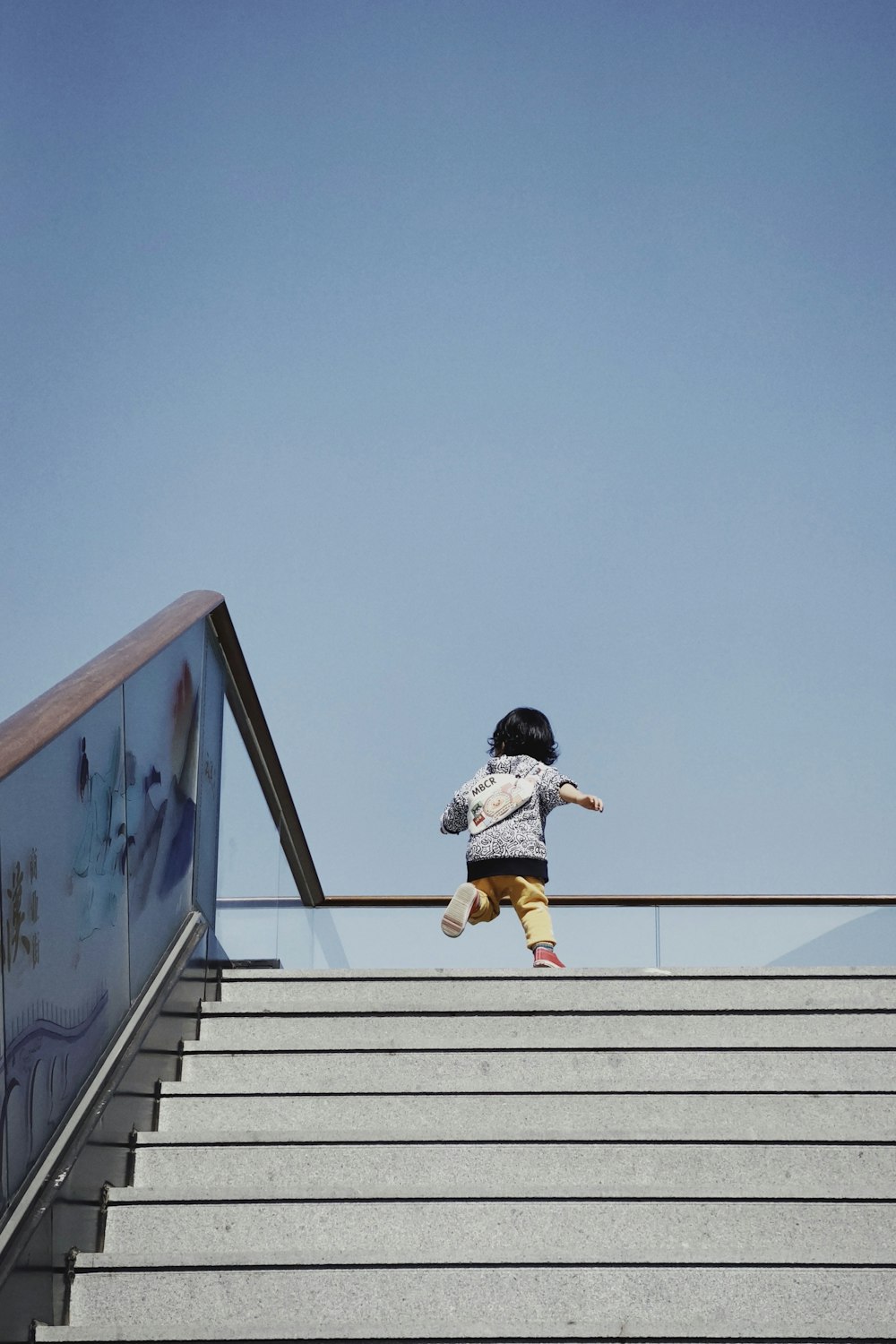 girl in white shirt and brown pants jumping on white concrete wall during daytime