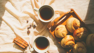 Cozy morning scene with a fresh cup of coffee and warm pastries on a wooden table.