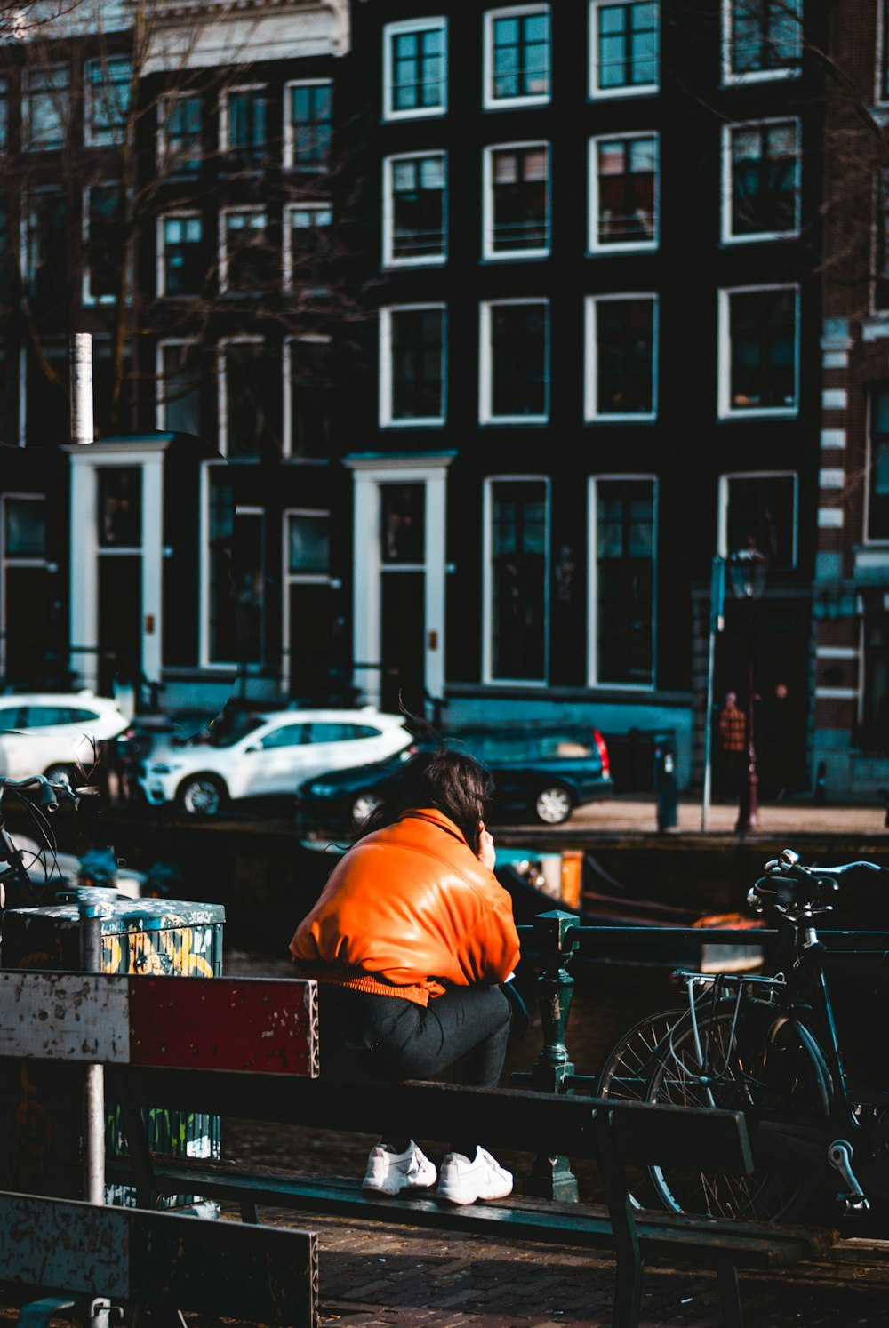 Mann im orangefarbenen Hemd sitzt tagsüber auf der Bank vor dem geparkten Fahrrad