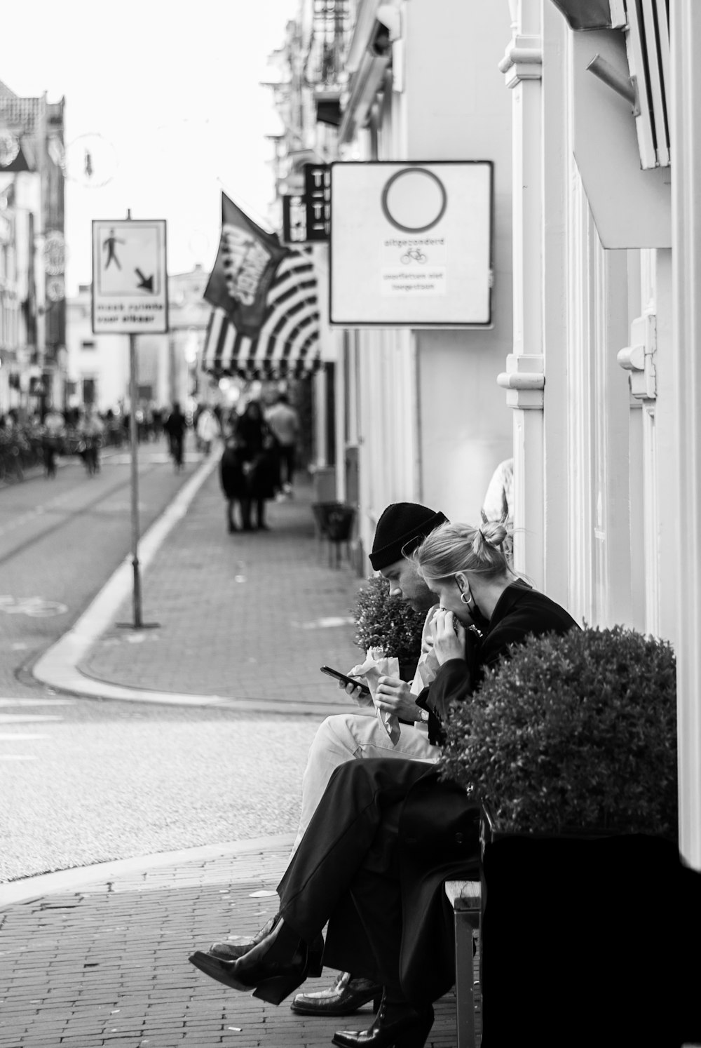 歩道に座っている黒いジャケットと黒いズボンの女性のグレースケール写真