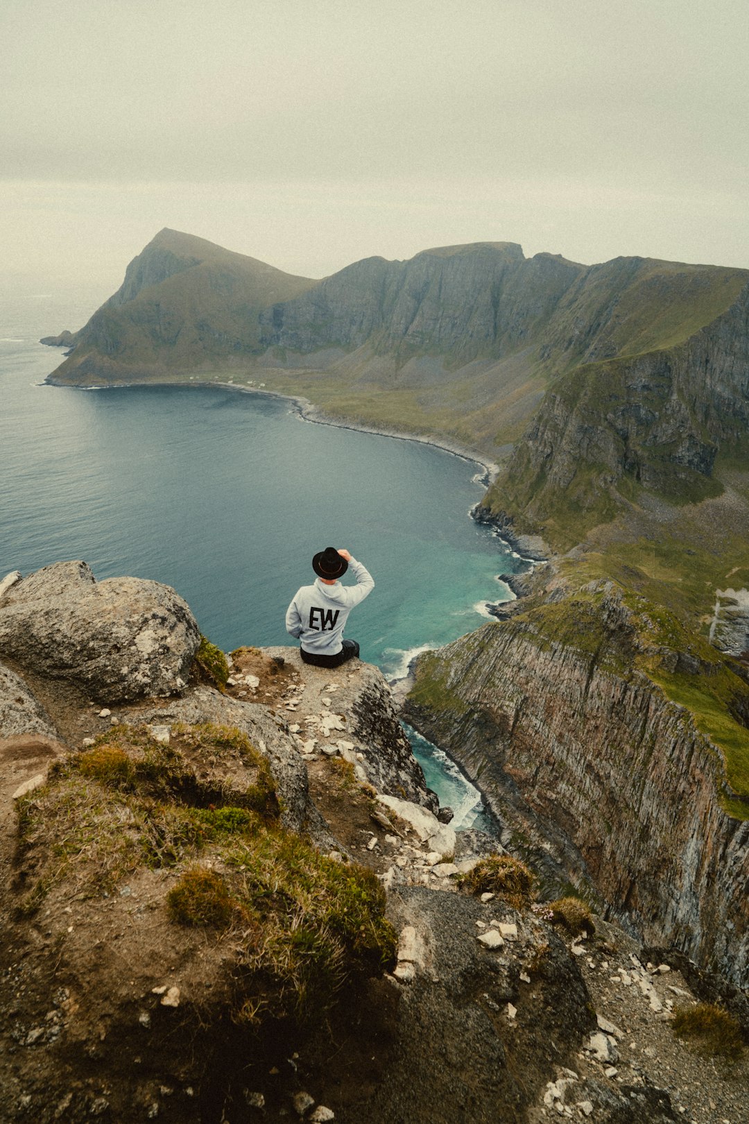 man in white shirt sitting on rock formation near body of water during daytime