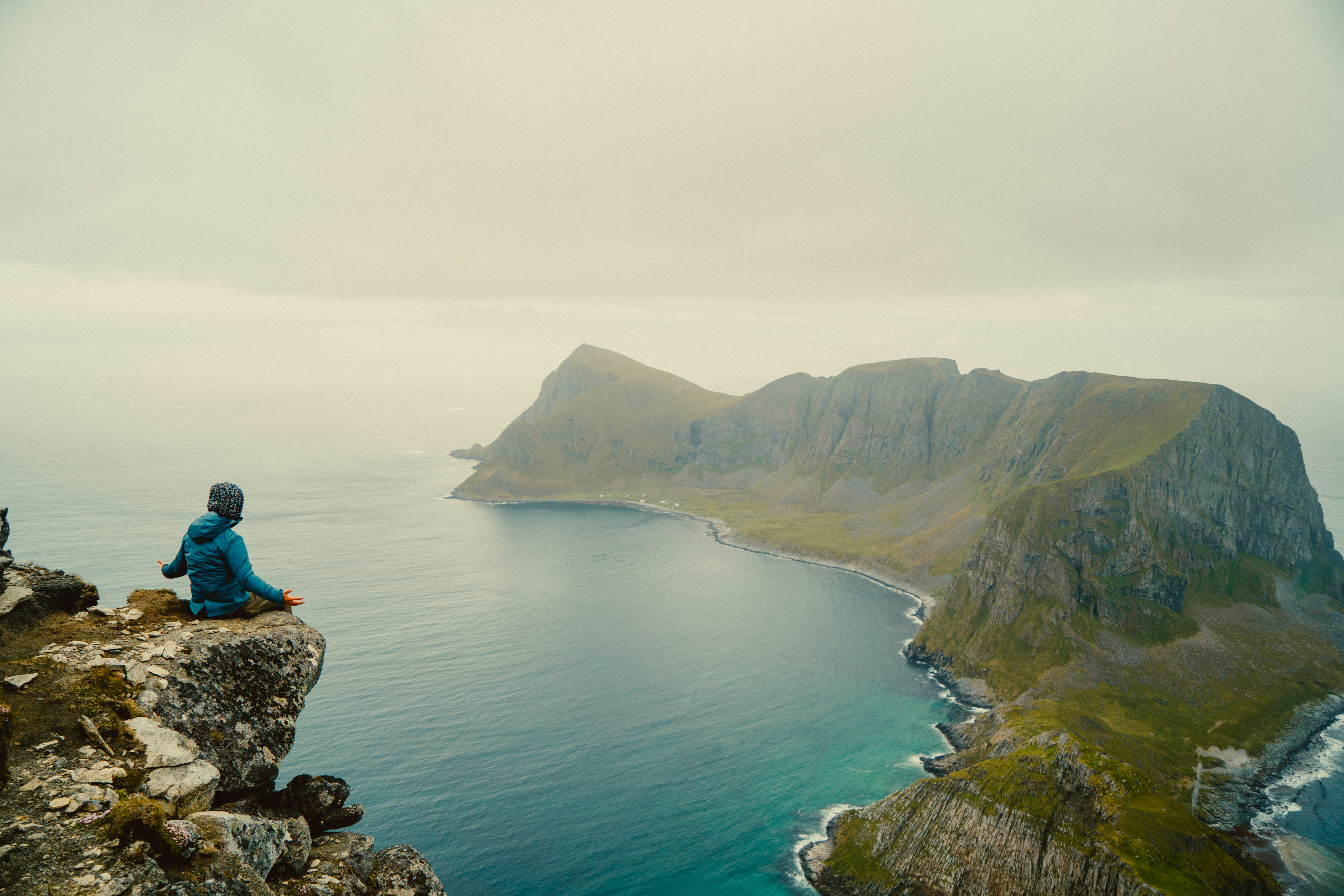 woman in blue jacket sitting on rock formation near body of water during daytime