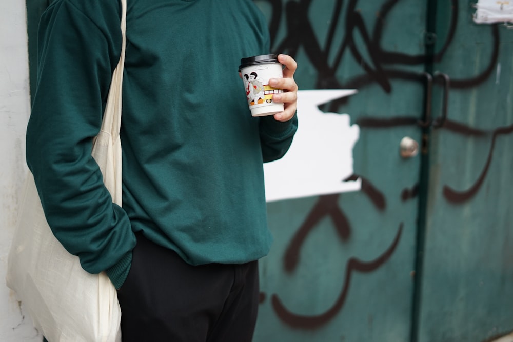 person in green sweater holding white ceramic mug