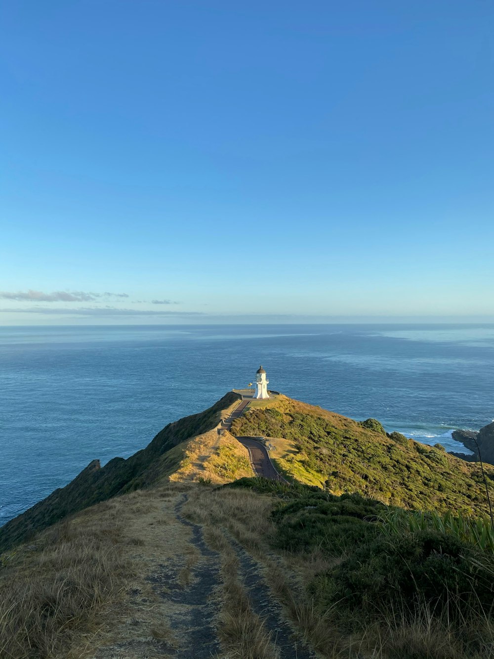 white lighthouse on top of hill by the sea under blue sky during daytime