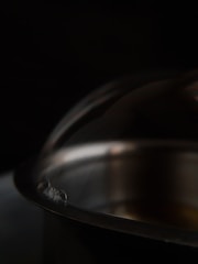 Close-up of a polished stainless steel pot reflecting soft factory lighting.