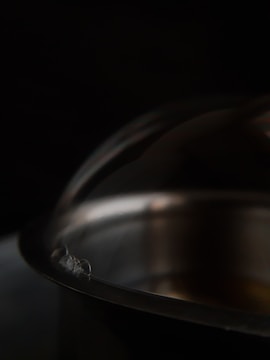 Close-up of a polished stainless steel pot reflecting soft factory lighting.