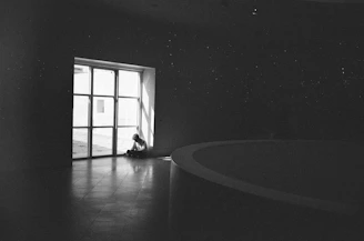 A person sitting alone in a dimly lit room, visibly overwhelmed and deep in thought.