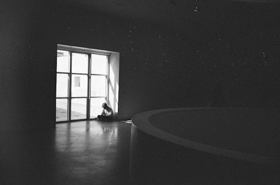 A person sitting alone in a dimly lit room, visibly overwhelmed and deep in thought.