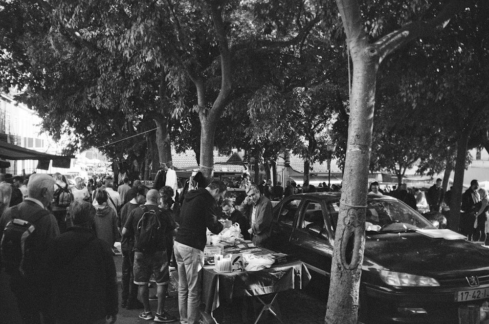 grayscale photo of people sitting on chairs near table and trees