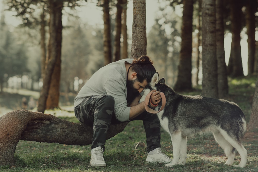 man in gray jacket hugging black and white siberian husky