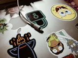 A funny sticker featuring a quirky character stuck on a laptop, with a matte forest green wall in the background.