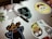 A collection of colorful cartoon character stickers is placed on a silver laptop surface. An assortment of stickers features animated characters and a charging cable draped over the laptop.