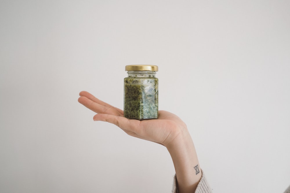 person holding green kush in glass jar